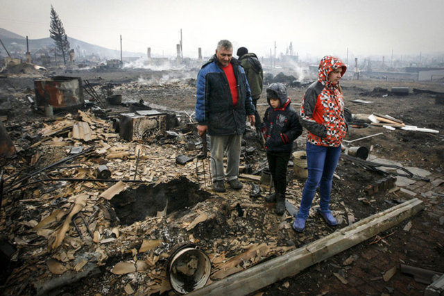 Local residents stand amidst the debris of a burnt building in the settlement of Shyra